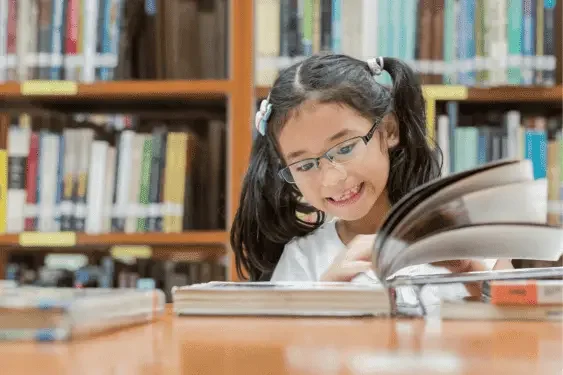 Image representing a student reading with a smile in a library